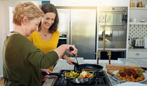 Mulheres felizes cozinhando após entender Como escolher cooktop.