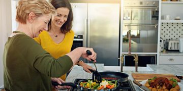 Mulheres felizes cozinhando após entender Como escolher cooktop.